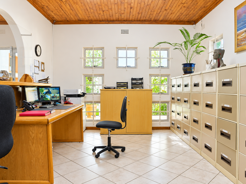 A well-maintained office space featuring a warm timber ceiling, tiled flooring, and extensive built-in filing cabinetry, providing a functional and organized professional work environment.