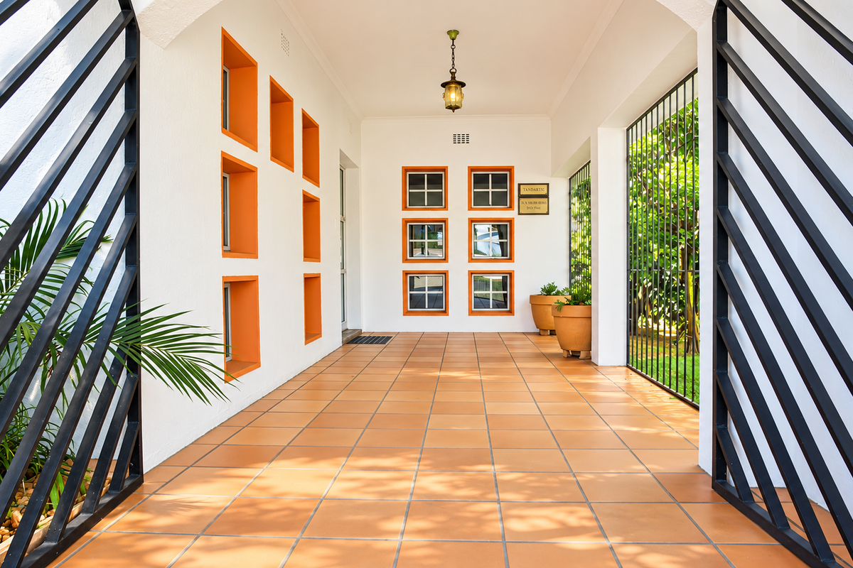 A well-maintained covered entrance area featuring terracotta tiled flooring, decorative orange-framed wall niches, and secure metal gate access.