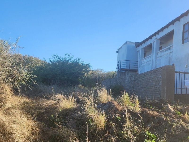 View of the rear exterior of the property featuring a boundary wall, metal gate, and elevated balcony area with overgrown surrounding land.