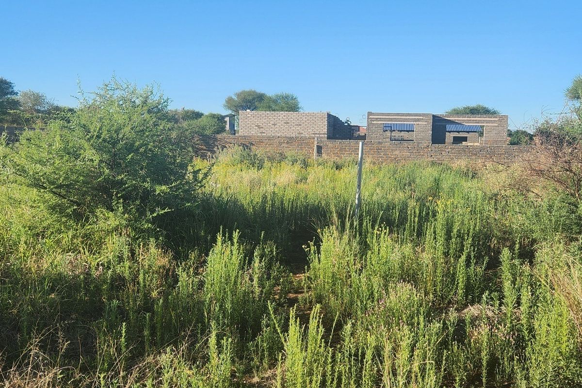 A vacant commercial land plot featuring overgrown vegetation and a partially constructed brick building structure at the rear.