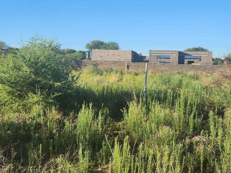 A vacant commercial land plot featuring overgrown vegetation and a partially constructed brick building structure at the rear.