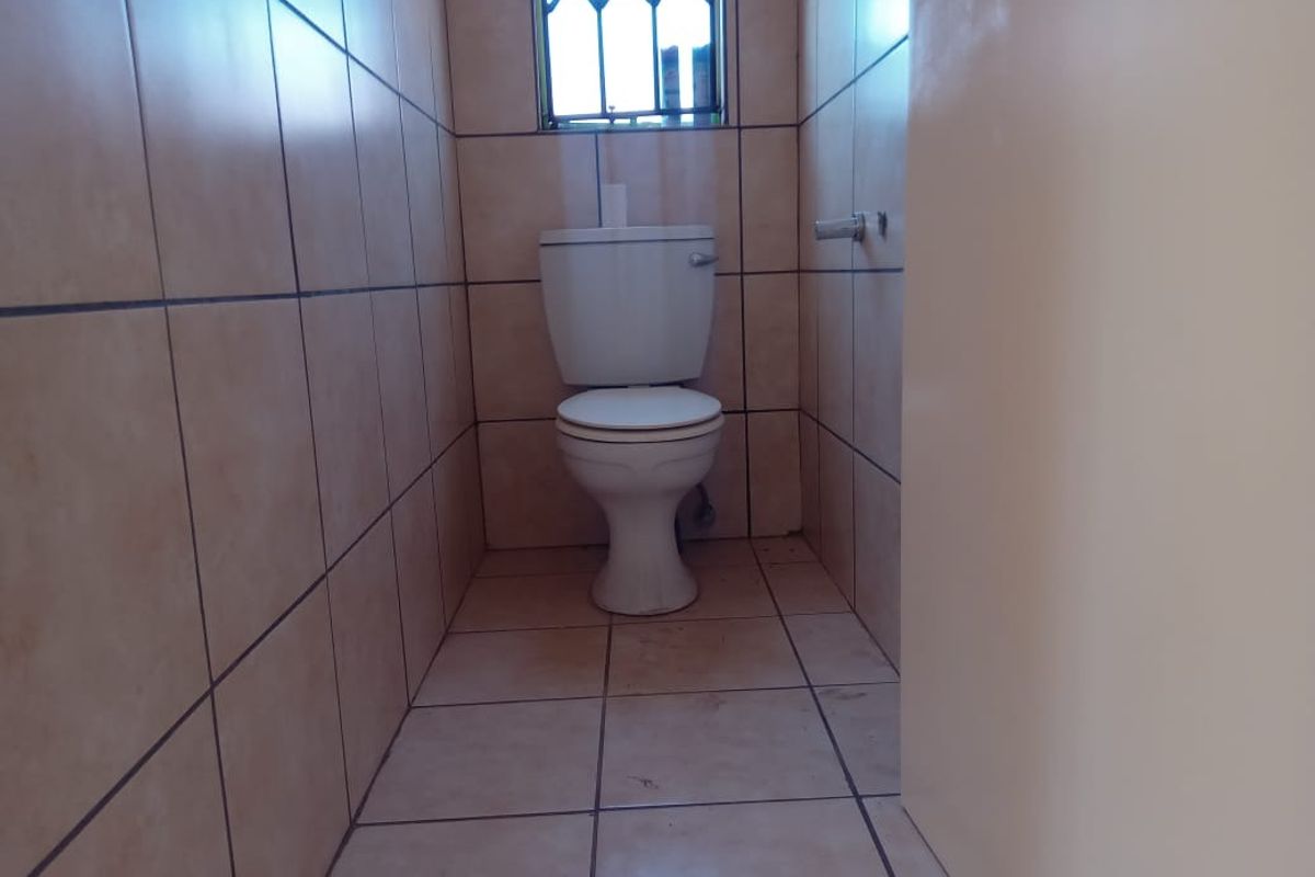A compact, tiled guest toilet featuring a standard white ceramic toilet suite and a small window with security bars.