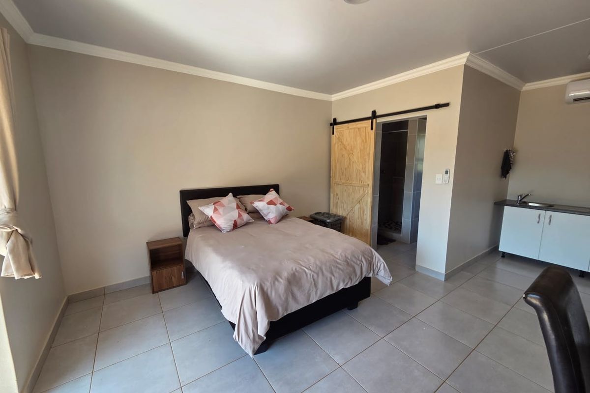 Open-plan studio apartment featuring tiled flooring, a kitchenette with sink, and a barn-style sliding door leading to an en-suite bathroom.