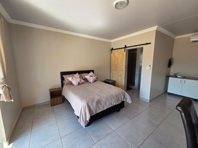 Open-plan studio apartment featuring tiled flooring, a kitchenette with sink, and a barn-style sliding door leading to an en-suite bathroom.
