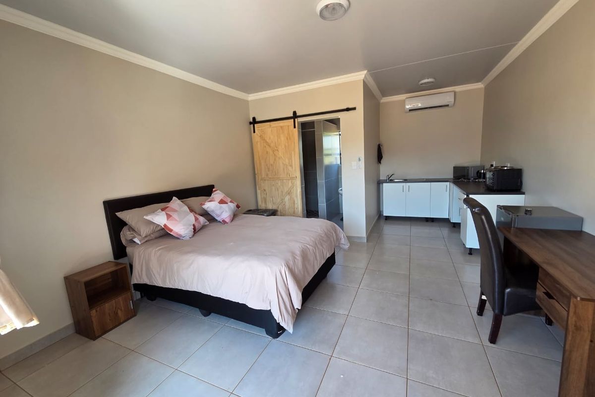 Open-plan studio apartment featuring tiled flooring, a kitchenette with built-in cabinetry, a barn-style door leading to the bathroom, and a wall-mounted air conditioner.
