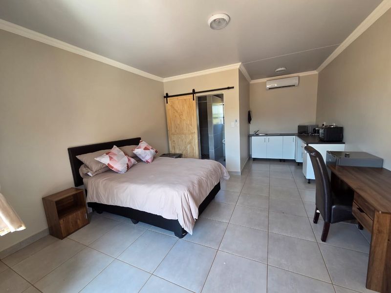 Open-plan studio apartment featuring tiled flooring, a kitchenette with built-in cabinetry, a barn-style door leading to the bathroom, and a wall-mounted air conditioner.