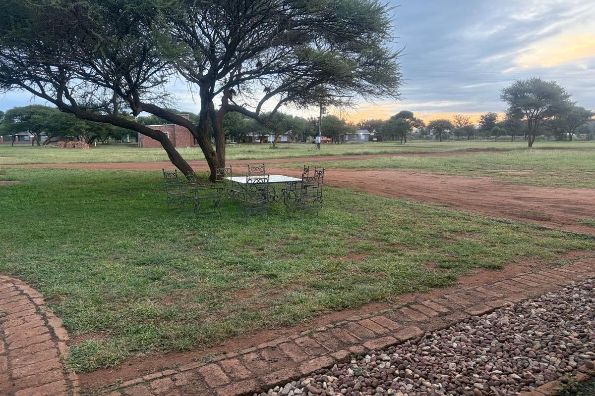 A spacious outdoor garden area featuring established trees, brick-paved pathways, and decorative pebble landscaping in a natural setting.