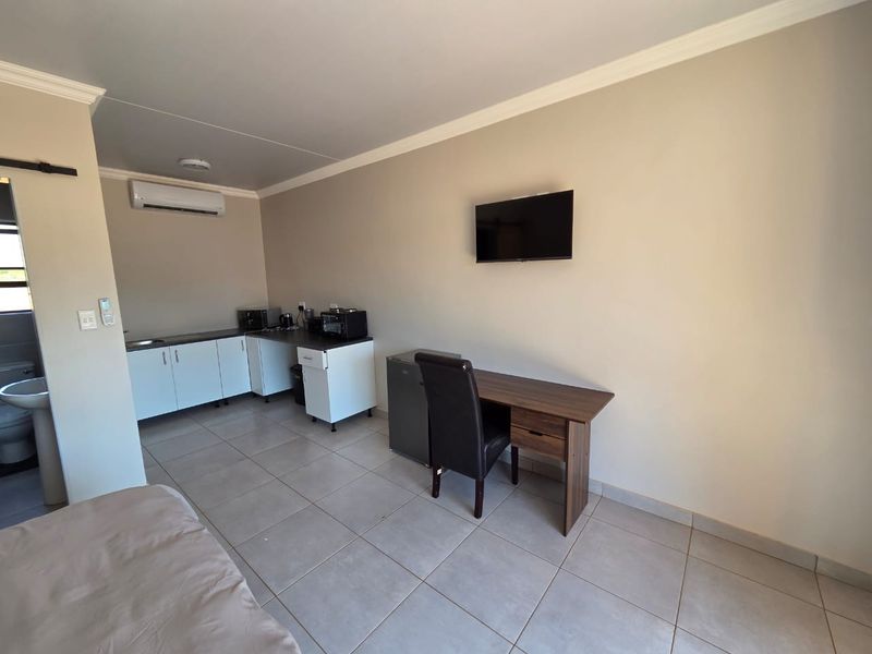 Open-plan studio apartment featuring a kitchenette with built-in cabinetry, tiled flooring, split-system air conditioning, and a wall-mounted television.