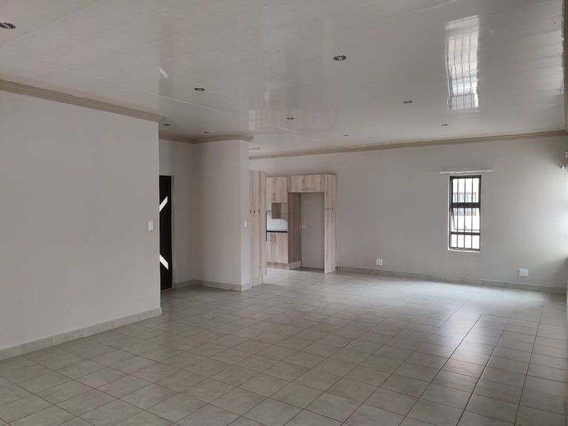 Spacious open-plan living area featuring neutral tiled flooring, recessed lighting, and a compact built-in kitchen unit with modern cabinetry.