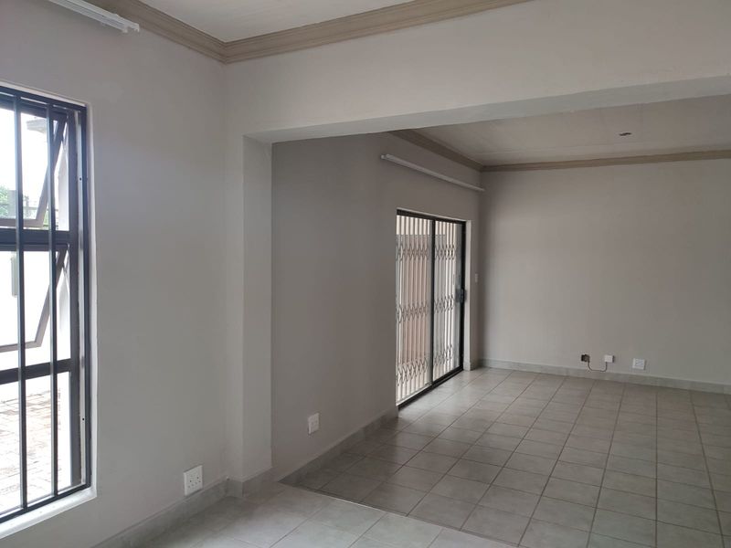 A bright, empty living area featuring neutral tiled flooring, coved ceilings, and a sliding glass door with a security gate leading outdoors.