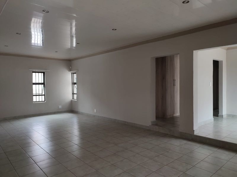 Spacious, empty living area featuring neutral tiled flooring, recessed downlighting, and security-fitted windows, leading into a secondary space with built-in storage.