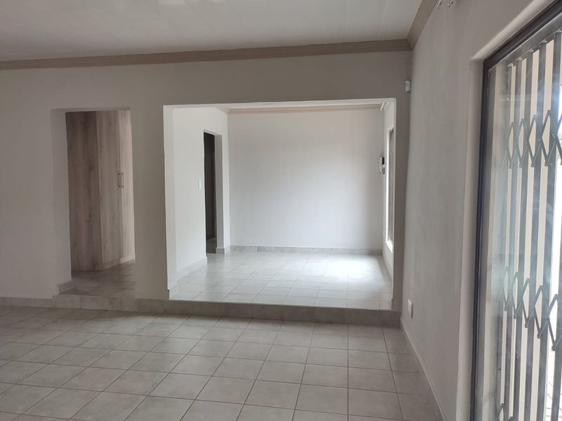 An empty, open-plan living area featuring neutral tiled flooring, built-in storage cupboards, and a secure metal gate at the entrance.