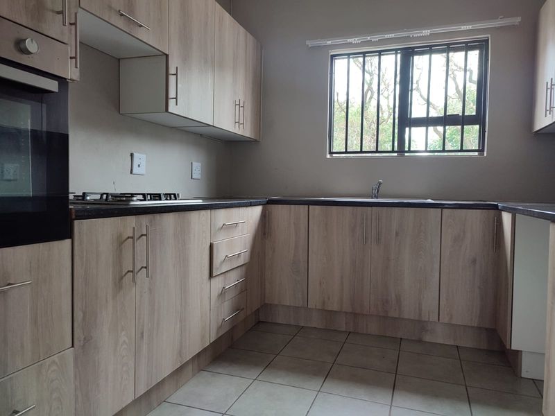A functional kitchen featuring light wood-look cabinetry, dark laminate countertops, a built-in oven, gas hob, and tiled flooring.