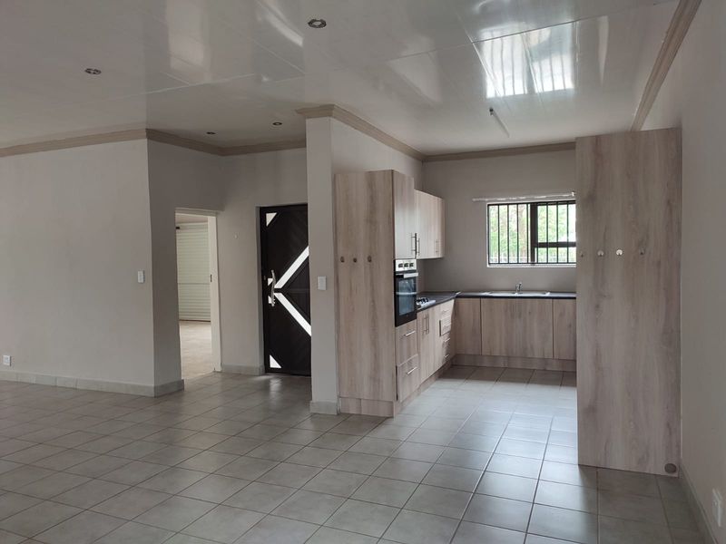 Open plan living area featuring a modern kitchen with built-in cabinetry, oven, and hob, finished with neutral tiled flooring and recessed lighting.
