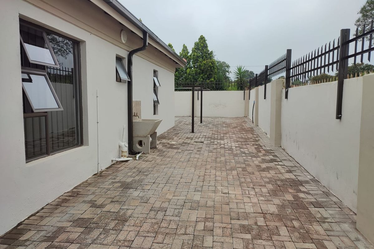 A paved rear courtyard featuring a perimeter wall with security spikes, a utility sink, and exterior wall access.