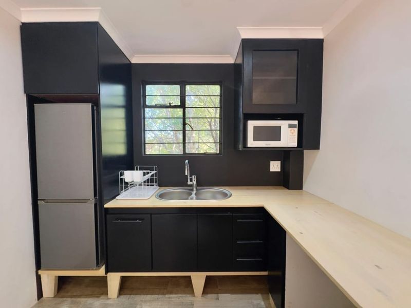 A compact kitchen featuring modern black cabinetry, light timber countertops, a double bowl sink, and a built-in microwave.