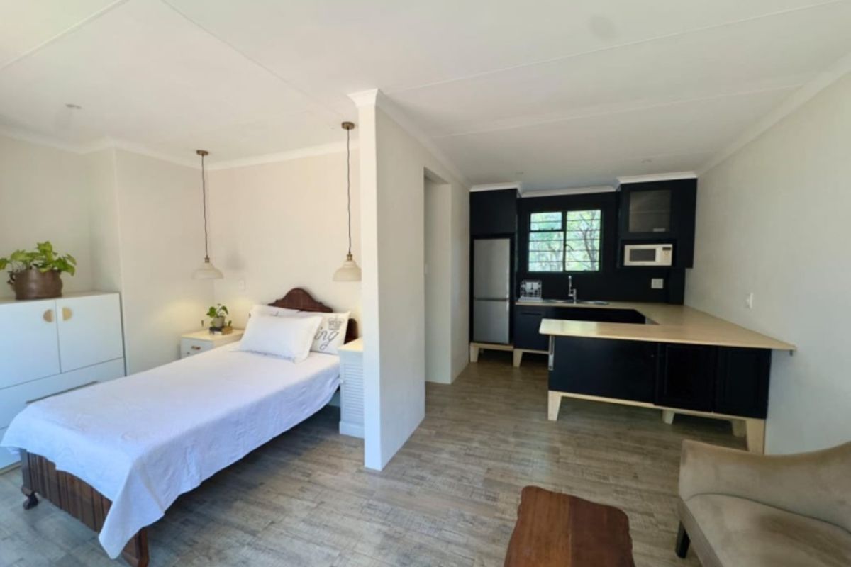 An open-plan studio apartment featuring a modern kitchen with dark cabinetry and a combined sleeping area with wood-look tile flooring throughout.