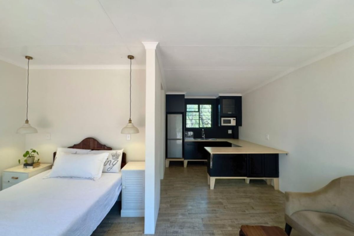 An open-plan studio apartment featuring a combined bedroom and kitchen area with modern dark cabinetry, light countertops, and wood-look laminate flooring.