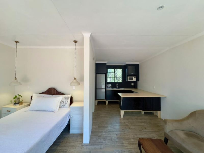 An open-plan studio apartment featuring a combined bedroom and kitchen area with modern dark cabinetry, light countertops, and wood-look laminate flooring.
