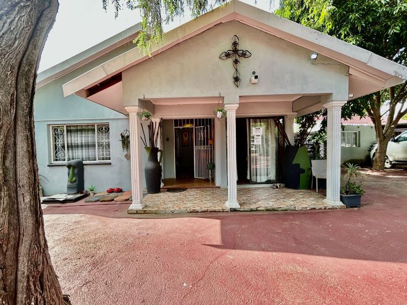 Front elevation of the apartment featuring a covered porch with decorative columns, security gate, and paved driveway access.