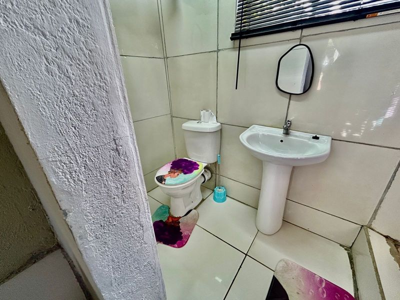 A compact bathroom featuring a pedestal washbasin, toilet, and tiled finishes. The space shows signs of wear and requires maintenance to the wall and floor.