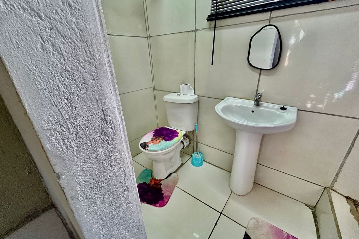A compact bathroom featuring a pedestal washbasin, toilet, and tiled finishes. The space shows signs of wear and requires maintenance to the wall and floor.