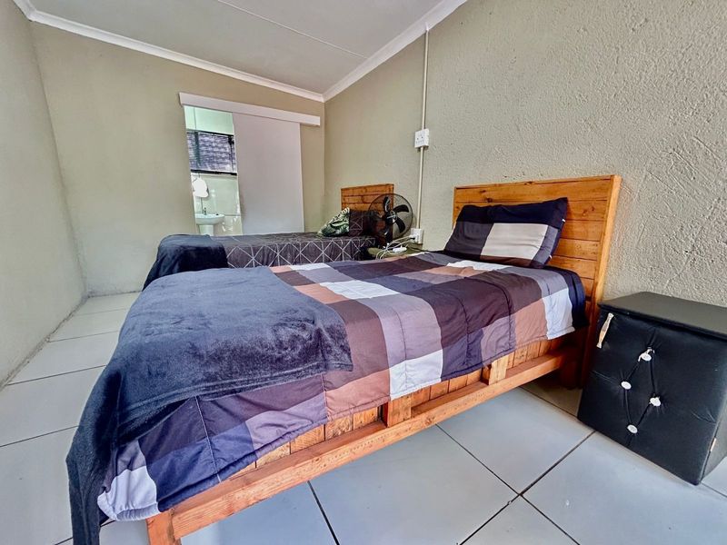 A functional bedroom featuring tiled flooring and a coved ceiling, with direct access to an adjoining bathroom area.