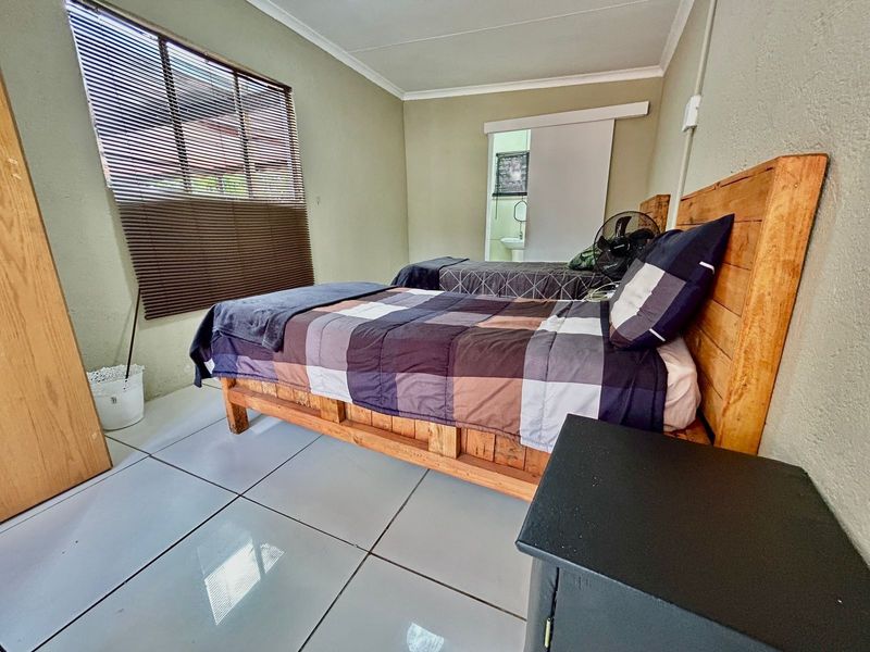 A functional bedroom featuring tiled flooring, a sliding door leading to an en-suite, and venetian blinds for privacy.