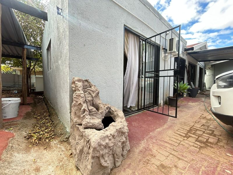 Rear exterior view of the apartment featuring a paved area, security gate, sliding door access, and an external air conditioning unit.
