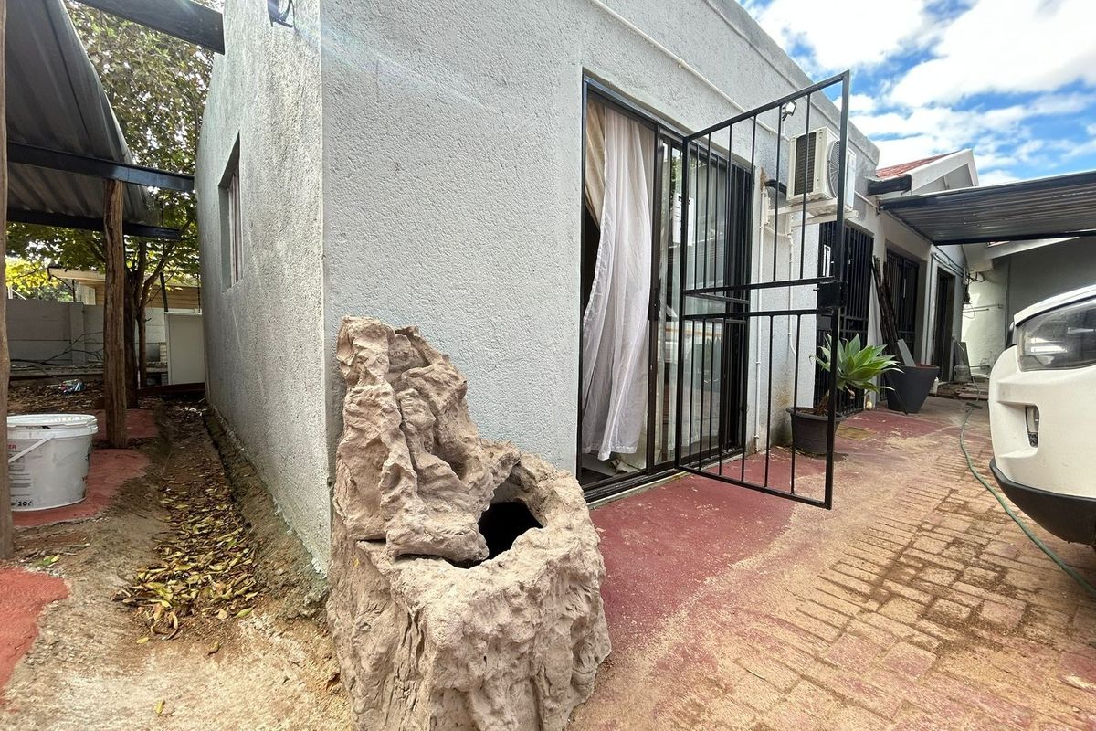 Rear exterior view of the apartment featuring a paved area, security gate, sliding door access, and an external air conditioning unit.