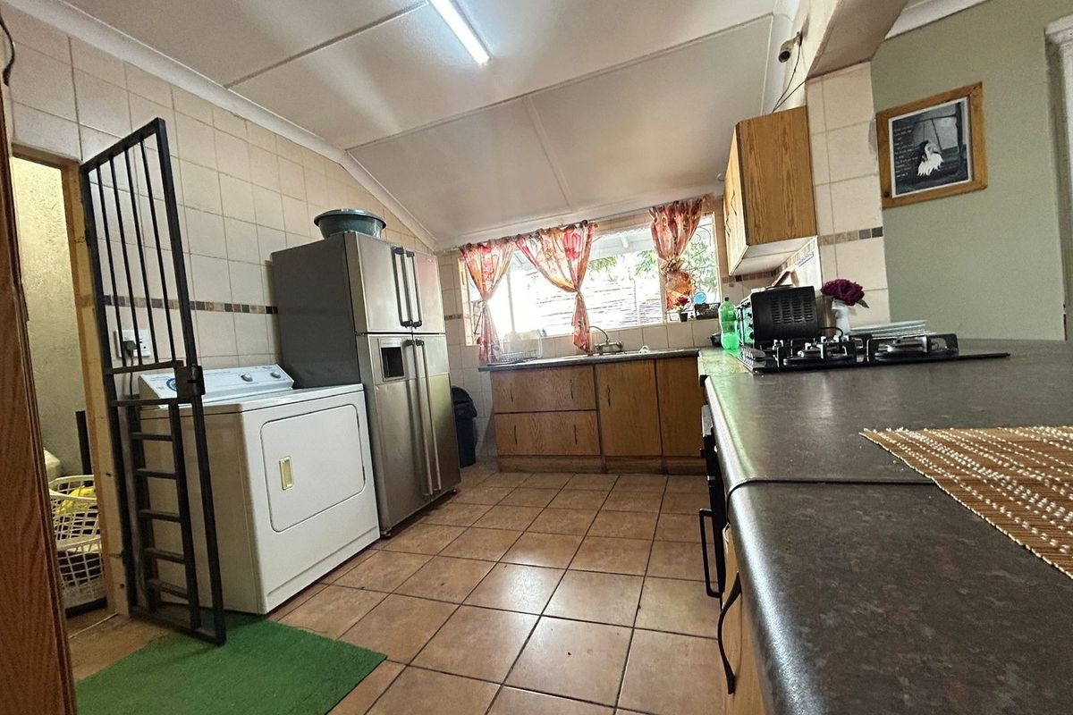 A functional kitchen featuring tiled flooring, built-in wooden cabinetry, a gas hob, and a stainless steel sink, requiring cosmetic updates to modernize the space.