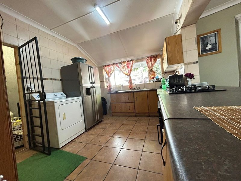 A functional kitchen featuring tiled flooring, built-in wooden cabinetry, a gas hob, and a stainless steel sink, requiring cosmetic updates to modernize the space.