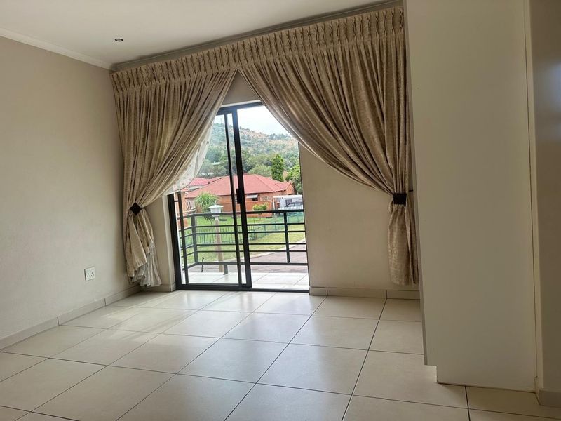 An empty living room featuring neutral tiled flooring and a large sliding glass door that opens to a balcony with scenic views.