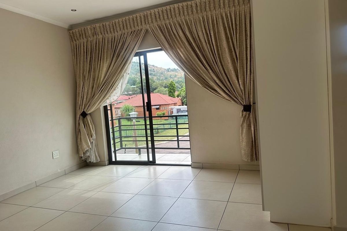 An empty living room featuring neutral tiled flooring and a large sliding glass door that opens to a balcony with scenic views.