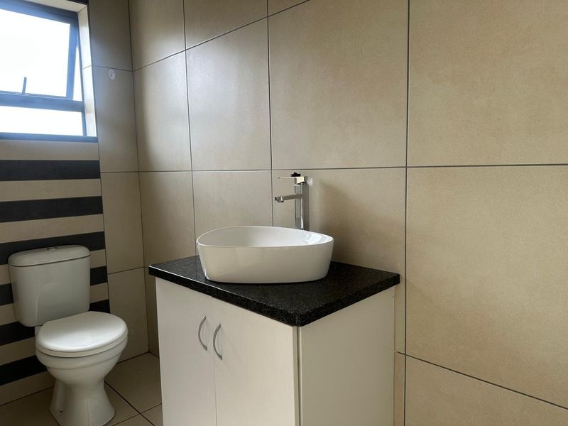 A clean and modern bathroom featuring a vessel sink on a granite-topped vanity, a toilet, and neutral ceramic wall and floor tiling.