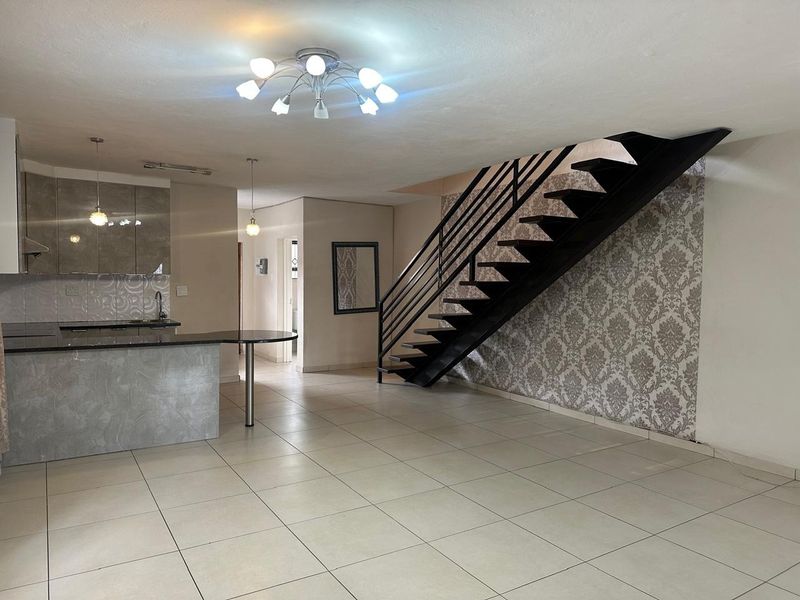 Spacious open-plan living area featuring a modern kitchen with granite countertops, tiled flooring, and a striking staircase with a metal handrail.