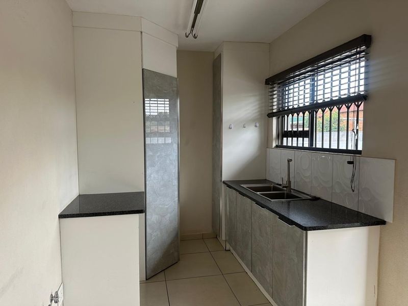 A functional scullery featuring built-in cabinetry, granite countertops, a double basin sink, and tiled flooring, providing a clean and practical workspace.