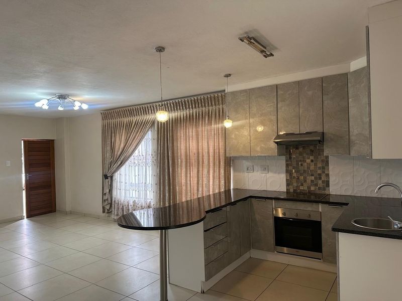 Open-plan kitchen and living area featuring modern grey cabinetry, granite countertops, built-in oven and hob, and neutral tiled flooring throughout.