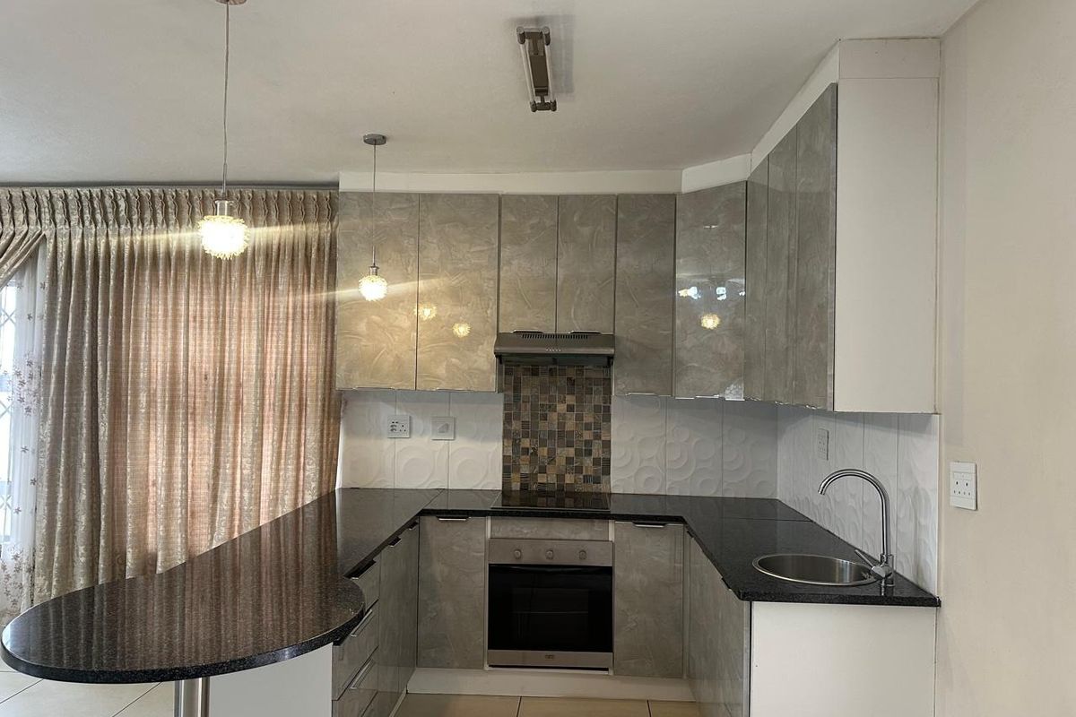 Modern kitchen featuring high-gloss cabinetry, granite countertops, integrated oven and hob, mosaic backsplash, and a breakfast bar peninsula.