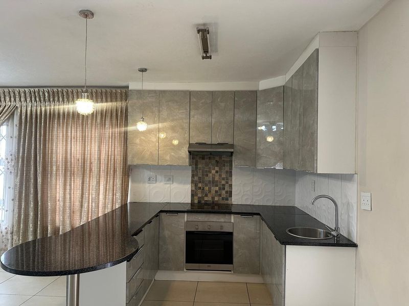 Modern kitchen featuring high-gloss cabinetry, granite countertops, integrated oven and hob, mosaic backsplash, and a breakfast bar peninsula.