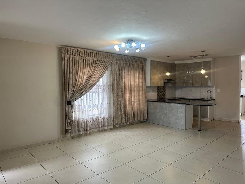 Spacious open-plan living and kitchen area featuring tiled floors, modern cabinetry, granite countertops, and a breakfast bar, offering a clean and functional layout.