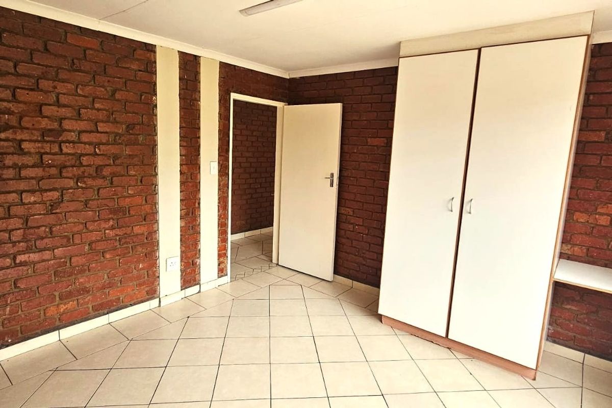 A vacant bedroom featuring exposed brick walls, tiled flooring, and a built-in wardrobe, offering a blank canvas for personalization.