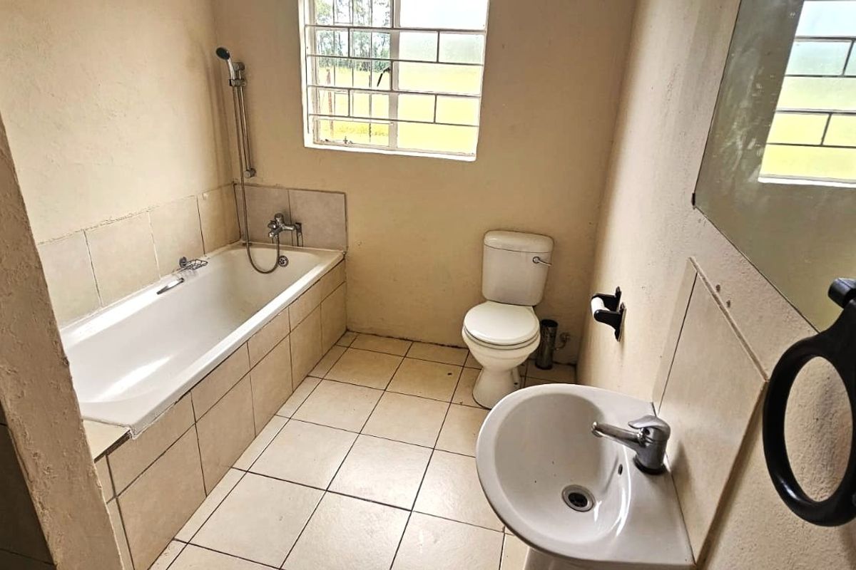 A functional bathroom featuring a bathtub, pedestal basin, and toilet, with tiled flooring and security bars on the window.