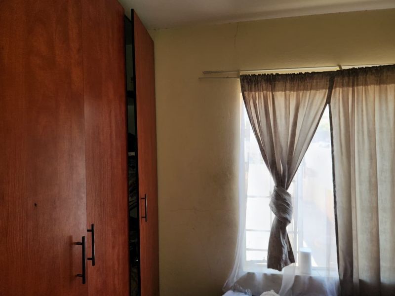 A bedroom featuring built-in wooden cupboards and a window with natural light, showing minor signs of wear on the wall.