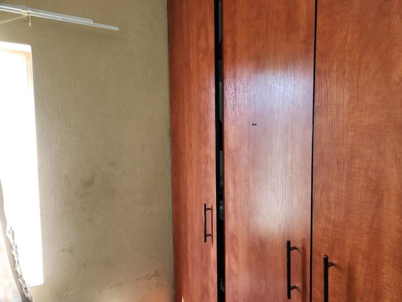 A bedroom featuring built-in wooden cupboards and a window, showing signs of wall staining and wear requiring maintenance.