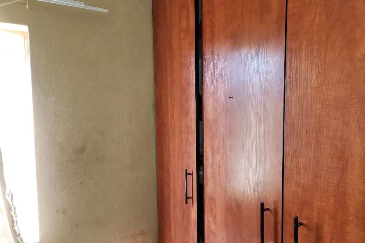 A bedroom featuring built-in wooden cupboards and a window, showing signs of wall staining and wear requiring maintenance.