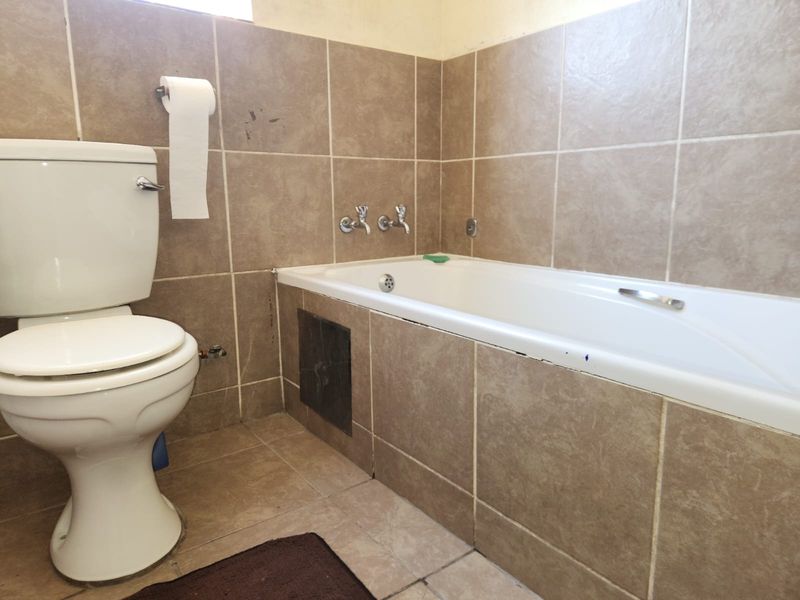 A functional bathroom featuring a built-in bathtub and toilet with neutral ceramic wall and floor tiling throughout.