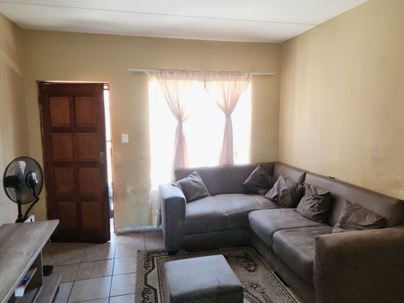 A living room featuring tiled flooring, a wooden entrance door, and a window, currently showing signs of wear on the walls and finishes.