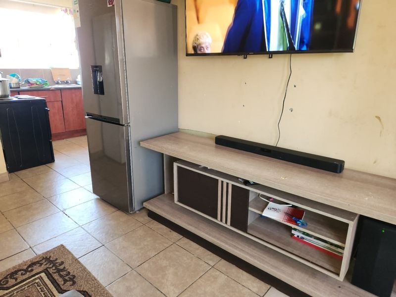 Open plan living area featuring tiled flooring and an adjacent kitchen space with built-in cabinetry and sink.