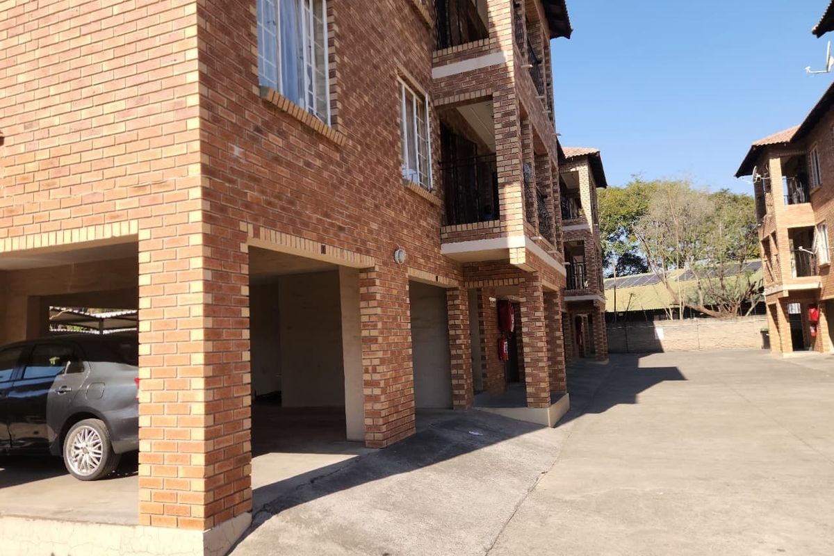 Exterior view of a multi-story apartment complex featuring face brick construction, covered ground-level parking bays, and private balconies.